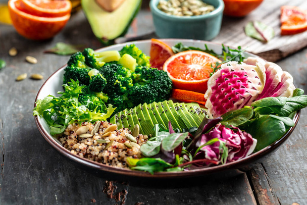 Quinoa vegetable vegetarian buddha bowl avocado, blood orange, broccoli, watermelon radish, spinach, quinoa, pumpkin seeds. top view. - Photo, Image