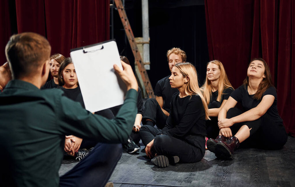 Sitting on the floor. Group of actors in dark colored clothes on rehearsal in the theater. - Foto, imagen