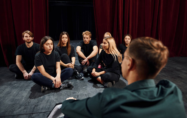 Sitting on the floor. Group of actors in dark colored clothes on rehearsal in the theater. - Photo, Image
