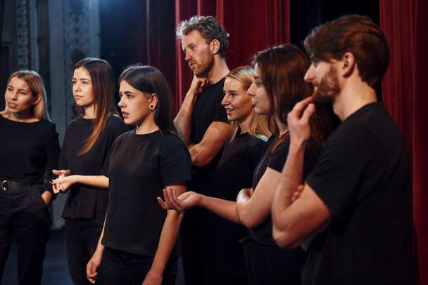 Side view. Group of actors in dark colored clothes on rehearsal in the theater. - Photo, image