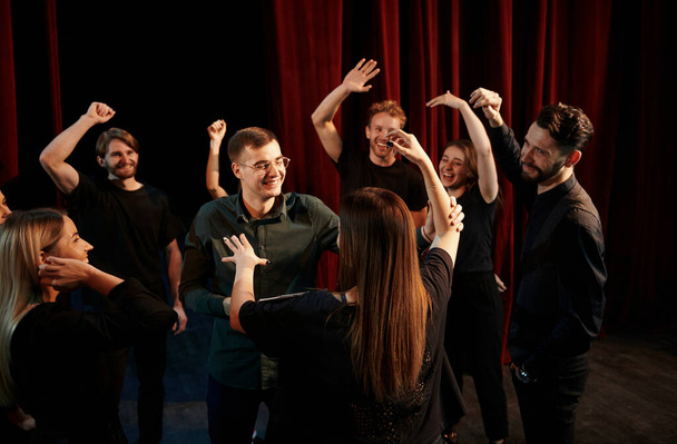 Happy people celebrating success. Group of actors in dark colored clothes on rehearsal in the theater. - Φωτογραφία, εικόνα