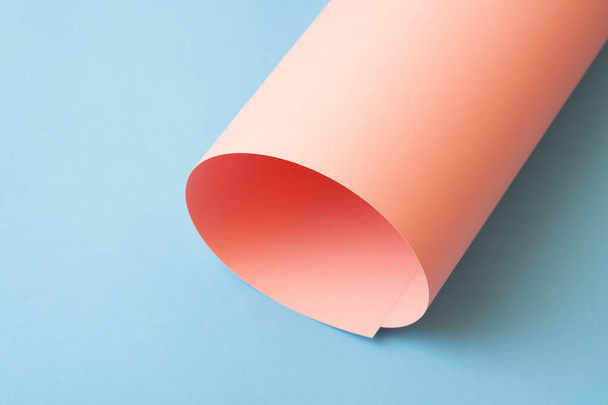 Rolled pink paper on blue background. - Zdjęcie, obraz