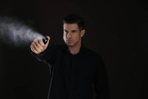 Man using pepper spray against black background, focus on hand - Photo, image
