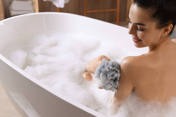Woman taking bath with mesh pouf in tub - Φωτογραφία, εικόνα