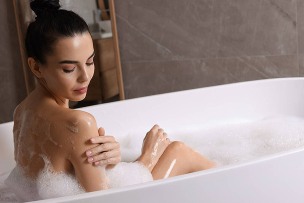 Woman taking bath with shower gel indoors - Фото, изображение