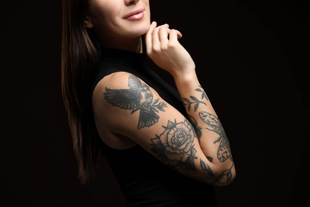 Woman with tattoos on arm against black background, closeup - Фото, зображення