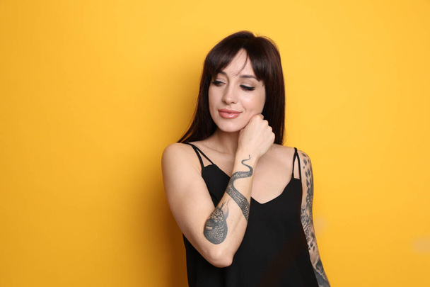 Beautiful woman with tattoos on arms against yellow background. Space for text - Foto, immagini
