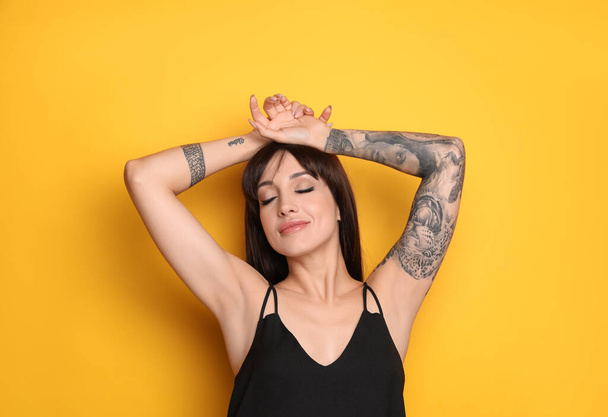 Beautiful woman with tattoos on arms against yellow background - Fotoğraf, Görsel