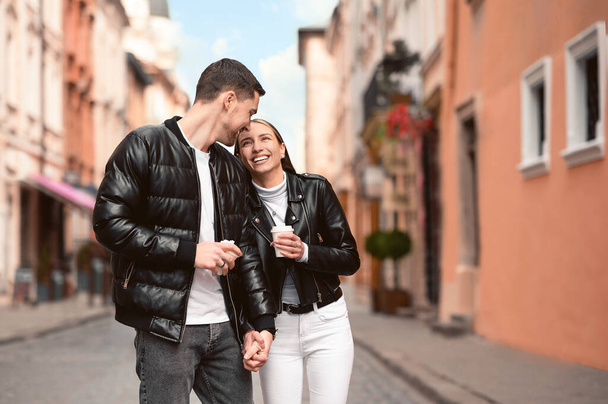 Lovely young couple with cups of coffee walking together on city street. Romantic date - Photo, image