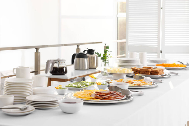 Clean dishware and different meals for breakfast on white table indoors. Buffet service - 写真・画像