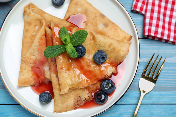Delicious crepes served with blueberries, mint and syrup on blue wooden table, flat lay - Valokuva, kuva