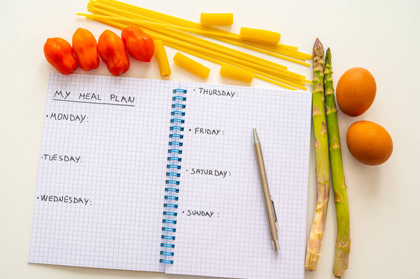 Page of notebook with black text "my meal plan", days of the week and next to it eggs, asparagus, pasta and tomatoes. Meal planning during the week. Diet and nutrition. - Photo, Image