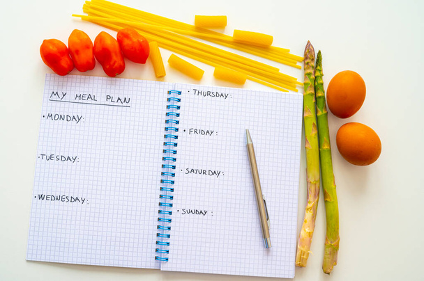 Page of notebook with black text "my meal plan", days of the week and next to it eggs, asparagus, pasta and tomatoes. Meal planning during the week. Diet and nutrition. - Foto, immagini