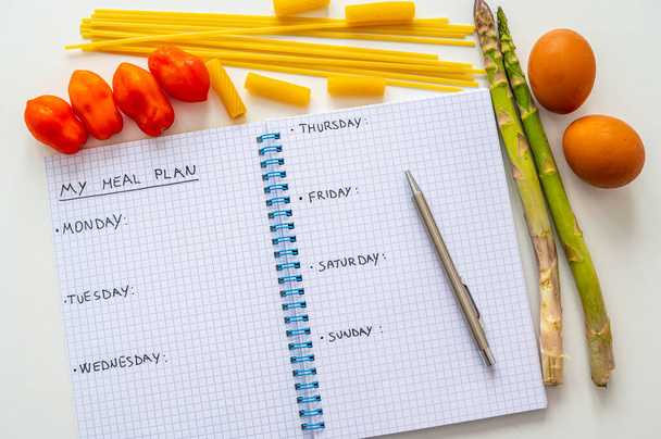 Page of notebook with black text "my meal plan", days of the week and next to it eggs, asparagus, pasta and tomatoes. Meal planning during the week. Diet and nutrition. - Foto, Bild