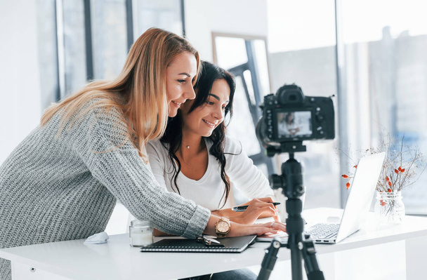 Camera on tripod is recording. Two young female freelancers working indoors in the office with laptop. - Fotografie, Obrázek