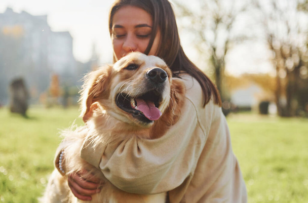 Embracing the pet. Young woman have a walk with Golden Retriever in the park. - 写真・画像