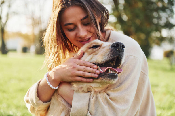 Embracing the pet. Young woman have a walk with Golden Retriever in the park. - Φωτογραφία, εικόνα