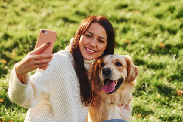 Making selfie. Young woman have a walk with Golden Retriever in the park. - Photo, Image