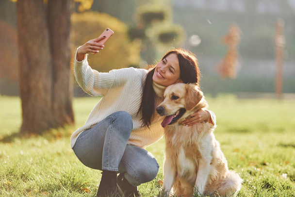 Making selfie. Young woman have a walk with Golden Retriever in the park. - Foto, Bild