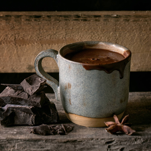 Cup of hot spicy homemade chocolate winter drink with chopped dark chocolate bar on old wooden shelf. Warm cozy drink. Square image - 写真・画像