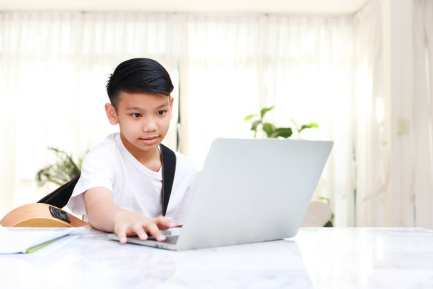 Asyalı çocuk evde dizüstü bilgisayarla müzik öğreniyor. İnternet üzerinden online eğitim kavramı. modern öğrenim - Fotoğraf, Görsel