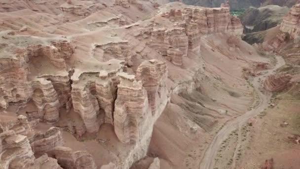 Grand Canyon Charyn-ban. Üledékes sziklákból származó kövek. Hatalmas repedések a sziklákon. A talaj vörös-narancssárga. Első látásra egy drónról. Van egy út a központban. A föld rétegei különböző színekben. - Felvétel, videó