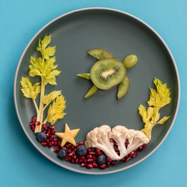 turtle, corals and plants in sea world from blackberries, kiwi, salad and cauliflower, isolated colorful food ideas on plate, copy space - Photo, Image