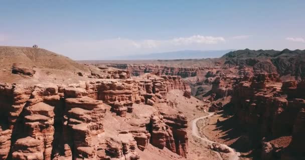 De Grand Canyon Charyn. Stenen van sedimentaire rotsen. Enorme scheuren in de rotsen. De grond is rood-oranje. Bovenaanzicht van een drone. Er is een weg in het centrum. Lagen van aarde in verschillende kleuren. - Video