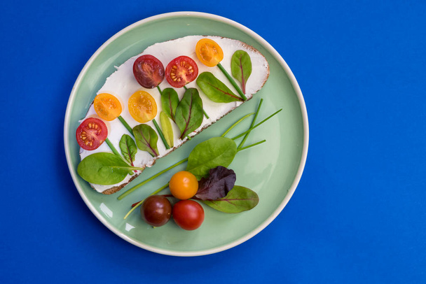 bread with butter, red and orange cherry tomatoes designed as flowers with green chives and basil herbs - Foto, Imagem