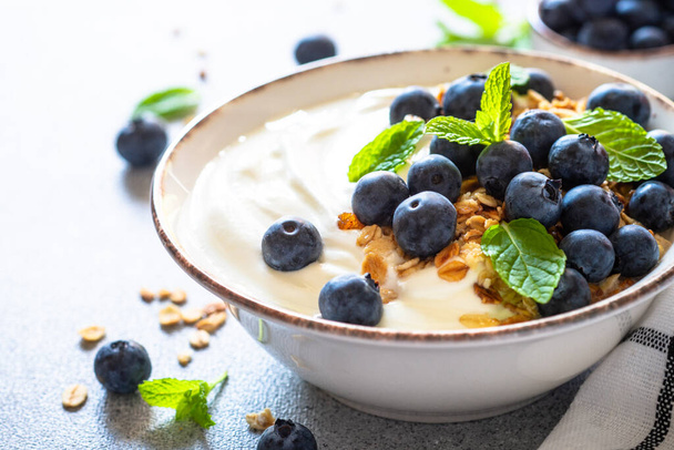 Griechischer Joghurt mit Müsli und frischen Blaubeeren an einem hellen Steintisch. Bild aus nächster Nähe. - Foto, Bild