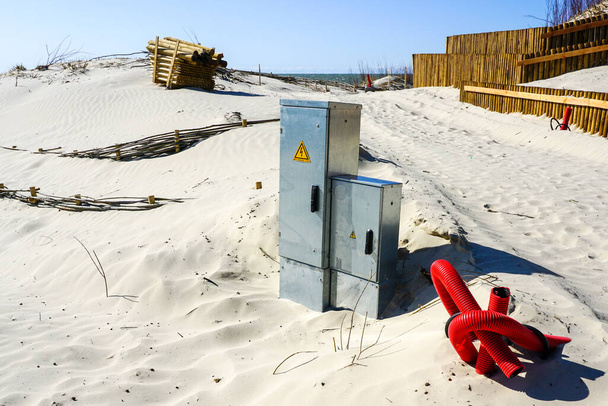 Két új kültéri fém elektromos kapcsolótábla és egy új világító lámpaoszlop betonalapja tápkábellel a homokos tengerparton - Fotó, kép