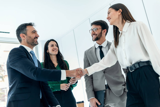 Shot of business people shaking their hands while smiling after signing new contract in modern startup office. - Zdjęcie, obraz