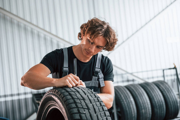 Fixes broken tire. Adult man in grey colored uniform works in the automobile salon. - Fotografie, Obrázek