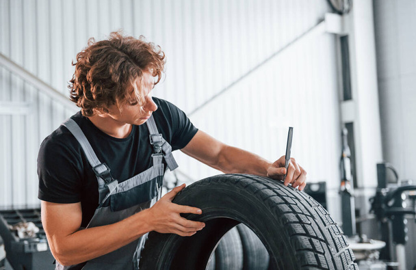 Fixes broken tire. Adult man in grey colored uniform works in the automobile salon. - Φωτογραφία, εικόνα