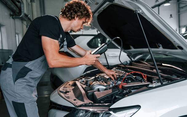 Tests car's electronics. Adult man in grey colored uniform works in the automobile salon. - Fotografie, Obrázek