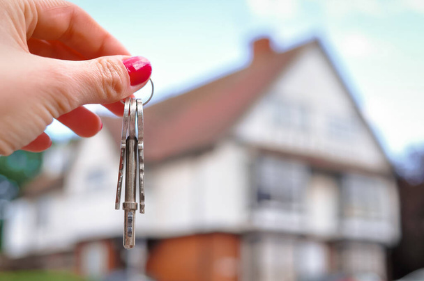Main de femme avec des clés en métal sur fond flou avec maison. Photo de haute qualité - Photo, image