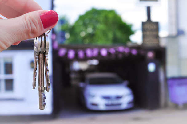 Woman's hand with metal keys on blurred background with house. High quality photo - Photo, Image
