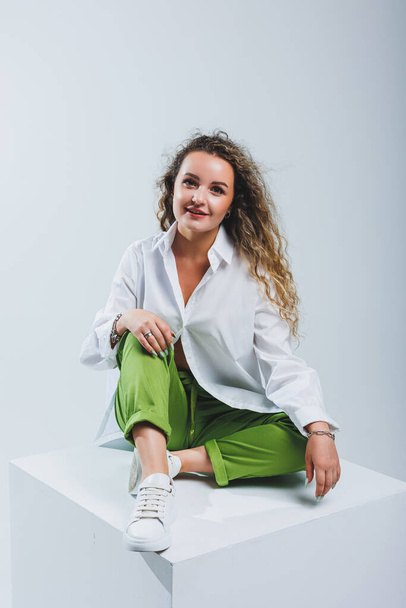 Positive woman with curly hair in a white light cotton shirt and trousers on a white isolated background. Women's casual wear. - Photo, Image