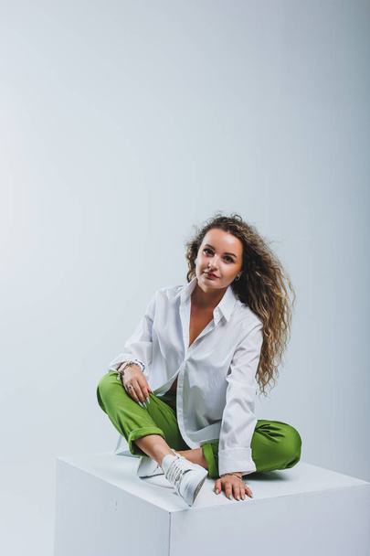 Positive woman with curly hair in a white light cotton shirt and trousers on a white isolated background. Women's casual wear. - Foto, imagen