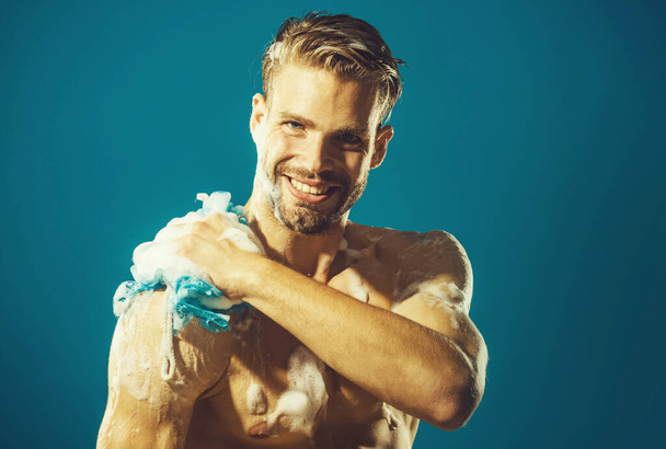 Улыбающийся мужчина моет тело увлажняющим гелем и мочалкой, принимая душ. Утренняя программа. СПА. - Фото, изображение