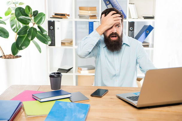 Frustated man clutching head working at laptop in office, frustration - Foto, Bild