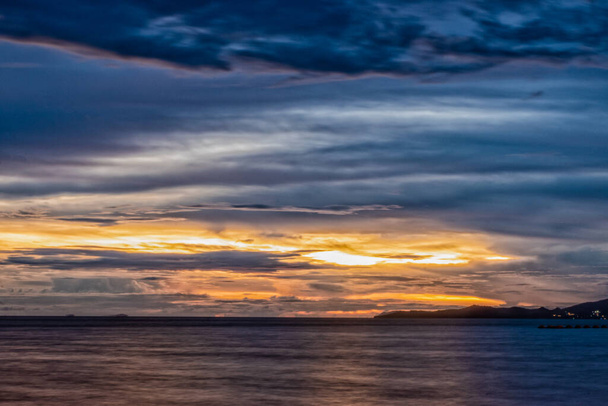 Ein tiefer und lebhafter Sonnenuntergang am Strand von Jomtien in Pattaya, Thailand. Die ferne Küste ist als Silhouette sichtbar und die Wolken sind dramatisch über dem dunklen Ozean. - Foto, Bild
