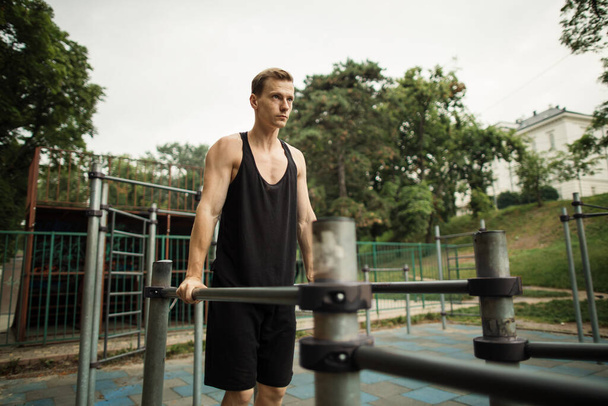 Fit man doing triceps dips on parallel bars at park exercising outdoors - Foto, Imagen