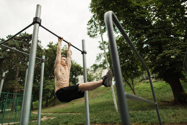 Young caucasian athlete with muscular torso doing corner on crossbar - Fotoğraf, Görsel