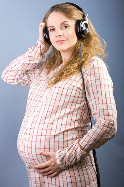 自宅でヘッドフォンで音楽を聴く若い妊婦の閉鎖。妊娠中の女性の肖像画 - 写真・画像