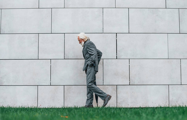 Hombre de negocios senior en ropa formal, con pelo gris y barba al aire libre camina con paraguas en la mano. - Foto, Imagen
