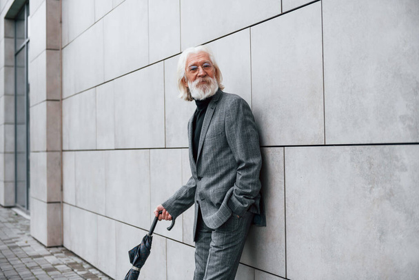 Holds umbrella. Senior businessman in formal clothes, with grey hair and beard is outdoors. - Foto, Imagem
