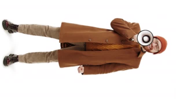 Vertical de cuerpo completo de un caucásico barbudo elegante hipster hombre en marrón ropa de otoño gritando alegremente a través de megáfono sobre fondo blanco. - Imágenes, Vídeo
