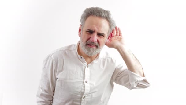 Старший сіро-волохатий білий чоловік у сорочці торкається його вуха і намагається почути, що хтось говорить на білому тлі. Проблеми зі здоров'ям у літньому віці
. - Кадри, відео