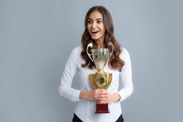 Portrait of happy young business woman with gold trophy cup on gray background. - Photo, Image